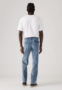 Witte katoenen T-shirt en lichtblauwe denim jeans. De jeans hebben een losse pasvorm, twee achterzakken en subtiele stikdetails.