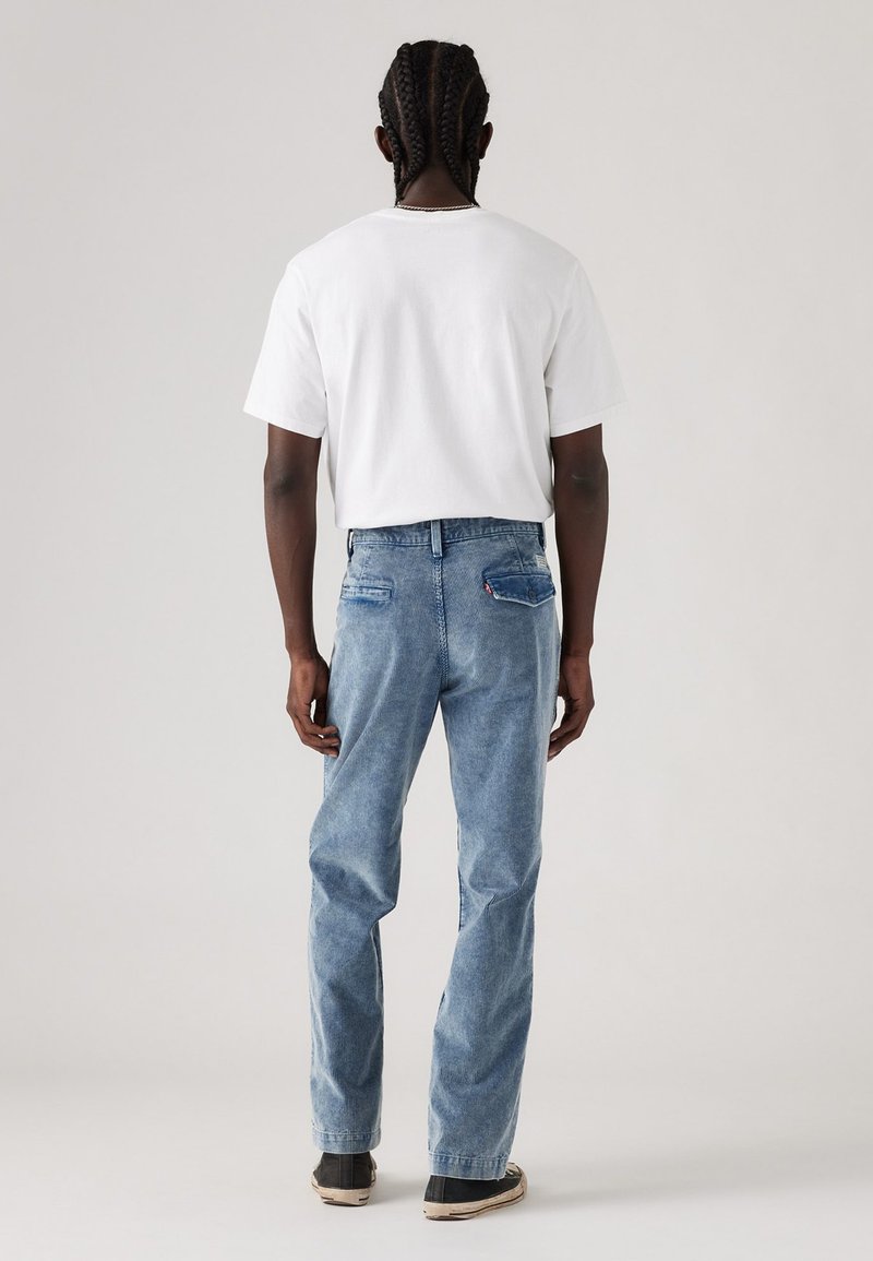 Weißes Baumwoll-T-Shirt und hellblaue Jeans. Die Jeans haben eine lockere Passform, zwei Gesäßtaschen und dezente Nähdetails.