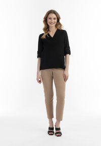 Sort V-hals top med rulleærmer, parret med brune, tætsiddende bukser og sorte høje sandaler. Glat tekstur og enkelt design.