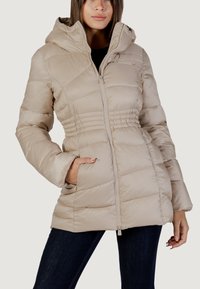 Giacca imbottita beige con chiusura zip, cappuccio e vita elasticizzata. Presenta cuciture diagonali e due tasche frontali. Tessuto liscio.