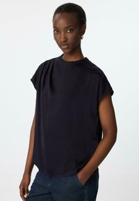 Marineblaues Kurzarmoberteil aus einem weichen Stoff mit subtiler Textur, mit Rundhalsausschnitt und lockerer Passform, kombiniert mit blauen Jeans.