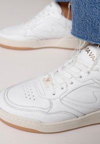 Weiße Ledersneakers mit perforierter Zehenkappe, beiger Gummisohle und flachen weißen Schnürsenkeln. Verfügt über ein Logodetail an der Seite und auf der Zunge.