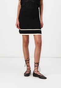 Black knit mini skirt with vertical ribbing, featuring a cream accent at the hem. Paired with black lace-up flats.