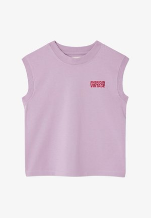 Jeune enfant aux cheveux mi-longs portant un débardeur violet clair et un short, chaussé de sandales beige, debout sur un fond uni.