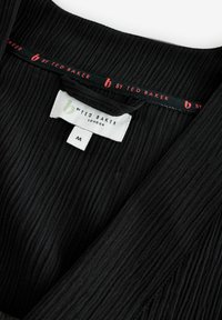 Zwarte textuurstof top met een v-halslijn, met het label "b by Ted Baker" in het rood aan de binnenkant van de hals. Het maatlabel geeft aan dat het medium is.
