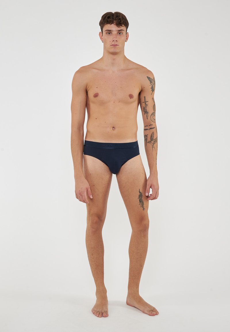 Marinblå bomullsboxer med mjukt midjeband, som har en slät yta och minimal sömnad. Modellen står barfota mot en neutral bakgrund.