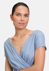 Robe bleu clair à manches courtes et décolleté en V profond. Le tissu a un léger éclat, créant une apparence texturée.