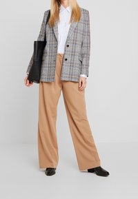 Żakiet w kratę w odcieniach szarości, niebieskiego i białego, dopasowany do sylwetki; w połączeniu z szerokimi beżowymi spodniami i czarnymi skórzanymi butami. W zestawie czarna torba typu tote.