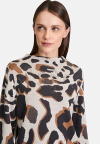 Knit sweater featuring a leopard print pattern in beige, brown, and black with a high neckline and varied textured accents.