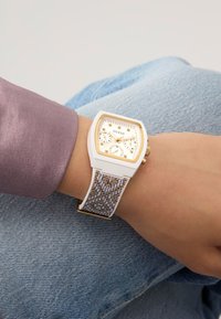 Montre Guess blanche avec un cadran rectangulaire, des accents dorés et deux cadrans ; bracelet à motifs gris et blanc ; finition lisse sur les matériaux.