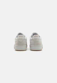 Zapatillas de ante gris con branding blanco en el talón, suela de goma texturizada y cuello acolchado, diseñadas con un estilo clásico de corte bajo.