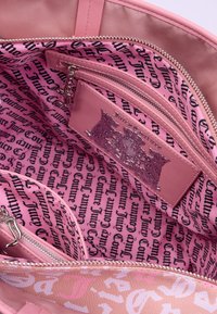Interno di una borsa rosa con tessuto morbido, molteplici scomparti, una sezione con zip e un motivo a testo ripetuto "Juicy Couture".