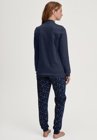Marineblauwe langemouwtop, van zachte stof, gecombineerd met marineblauwe pyjamabroek met witte maanfiguren en cuffs bij de enkels.