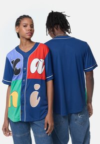Tricou colorat cu mânecă scurtă și deschidere cu nasturi, având secțiuni în violet, roșu, verde și albastru, cu text mare și jucăuș și accente albe.