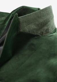 Grüner Wildlederstoff mit strukturiertem Finish, versehen mit einem stabilen Kragen und glatten Nähten. Das Material wirkt weich und strapazierfähig.