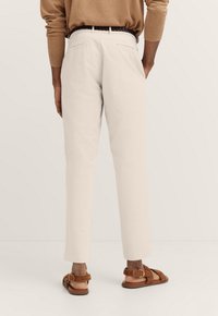 Helle beige Baumwollhose mit geraden Beinen, Gesäßtaschen und einem strukturierten schwarzen Gürtel. Getragen mit braunen Sandalen aus einem weichen Material.