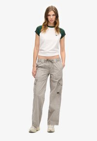 Weißes T-Shirt mit grünen Ärmeln, kombiniert mit hellgrauen Cargo-Hosen, die seitliche Taschen und einen Kordelzugbund haben. Legere Schuhe runden den Look ab.