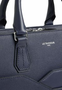 Bolso de mano de cuero marino con superficie texturizada, con un diseño geométrico, herrajes plateados y logo grabado en la parte frontal.