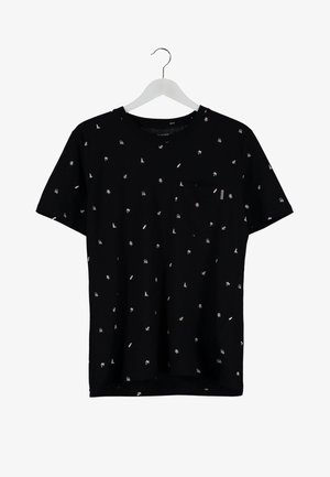 Man draagt een zwart bedrukt t-shirt, blauwe versleten jeans, zwarte sneakers, met een zwarte rugzak over één schouder, lopend naar voren.