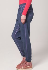 Marine joggebukser med avslappet passform, med lilla side-striper, mansjetterte ankler, og snøring i midjen, akkompagnert av rosa høye sneakers.