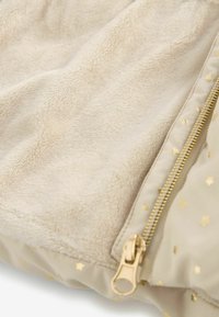 Beige fleece tæppe med en blød tekstur, en guldfarvet lynlås og små guldstjernemønstre langs kanten.