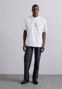 Weißes kurzärmliges T-Shirt mit grafischen Drucken und Rundhalsausschnitt, kombiniert mit dunklen Jeans aus Denim mit kontrastierenden Nähten und einer lockeren Passform.