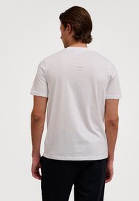Hvid kortærmet t-shirt med rund hals, glat tekstur, afslappet pasform, der har et mærkeområde på bagsiden og minimale syninger.