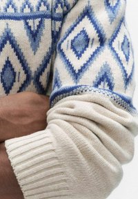 Neulottu paita, jossa on geometrinen sinivalkoinen timanttikuvio, resorit hihoissa ja pehmeä, teksturoitu pinta.