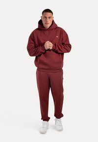 Burgundowa bluza z kapturem i dopasowane dresy, wykonane z mieszanki bawełny, z prążkowanymi mankietami i kieszenią z przodu. Białe sneakersy dopełniają strój.