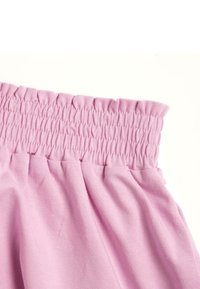 Tessuto rosa chiaro con una vita arricciata e una morbida texture; presenta delicate pieghe sotto la vita.