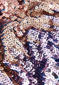 Sötét háttéren kör alakú rózsaarany és rózsaszín flitterekkel díszített anyag, texturált és tükröződő felületet létrehozva.