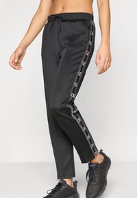 Μαύρο παντελόνι φόρμας με ελαστική μέση με κορδόνι, στενή γραμμή και αντίθετες πλευρικές ρίγες με κυκλικά διακοσμητικά στοιχεία και λεία υφή υφάσματος.