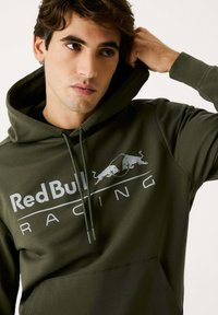Sudadera verde oliva de tejido suave, con un bolsillo frontal tipo canguro, capucha con cordón y un destacado logo blanco de "Red Bull Racing".