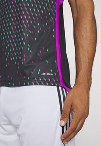 AEROREADY sportströja i svart med ett diamantmönster i grönt och lila. Har lila detaljer på sidorna och är tillverkad av ett andningsbart material.