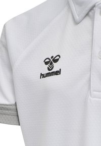 Witte polo met een gestructureerde stof, grijze accenten op de mouwen en een zwart 'hummel' logo op de borst. Drie-knopen sluiting.