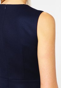 Vue arrière d'une personne portant une robe sans manches bleu marine foncé avec une fermeture éclair visible en haut au centre du dos.