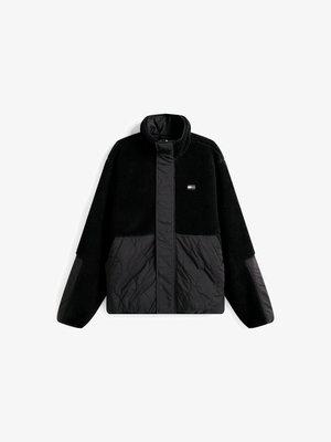Musta fleece-takki korkean kauluksen ja quiltattujen mustien paneelikoristeiden kanssa, rento istuvuus. Huomattava pehmeä tekstuuri ja minimaalinen brändäys.