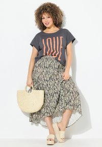 Graues T-Shirt mit orangefarbener "LOVE"-Schrift, kombiniert mit einem gemusterten Maxirock in Creme und Schwarz; geflochtene runde Tasche und beigefarbene Plateausandalen.
