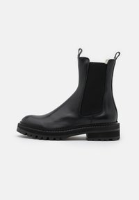 Botín Chelsea de cuero negro con paneles laterales elásticos, lengüetas, suela resistente y acabado texturizado para durabilidad y agarre.