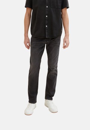Jeans din denim negru cu croi drept, purtați cu o cămașă neagră cu nasturi și adidași albi, expuși pe un fundal neutru.
