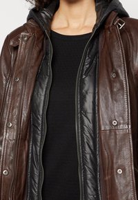 Brun läderjacka med avtagbar svart quiltad foder. Har silverfärgade tryckknappar, dragkedja fram och texturerade tygdetaljer.