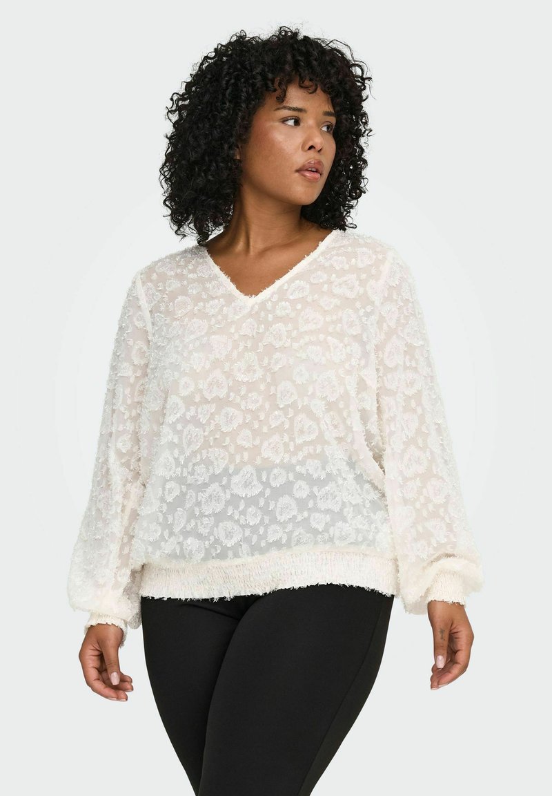 Bijela prozirna bluzica s cvjetnim uzorkom, V-izrezom, dugim rukavima i mekim, plišanim rubom; uparena s crnim tajicama koje lijepo prate tijelo.