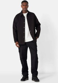 Black denim shirt with a collared design, snap buttons, worn over a white t-shirt. Paired with black cargo pants featuring side pockets.