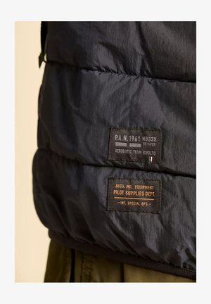 Giacca a vento nera con due etichette in tessuto: una con testo bianco e rosso e l'altra marrone, che recita "AUT. MIL. EQUIPMENT."