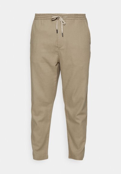 Calças de linho bege com um cós elástico e cordão. Corte afunilado com bolsos laterais e uma textura suave.