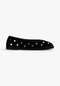 Zapato plano negro con tachuelas plateadas redondas y un pequeño emblema de calavera cerca del talón, mostrado de lado sobre un fondo blanco.