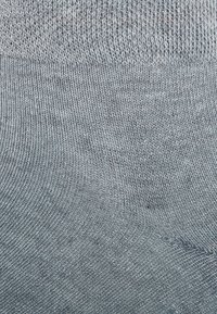 Graue gestrickte Socken mit einer glatten Textur, die einen gerippten Bund und ein diagonales Muster nahe der Oberseite aufweisen.