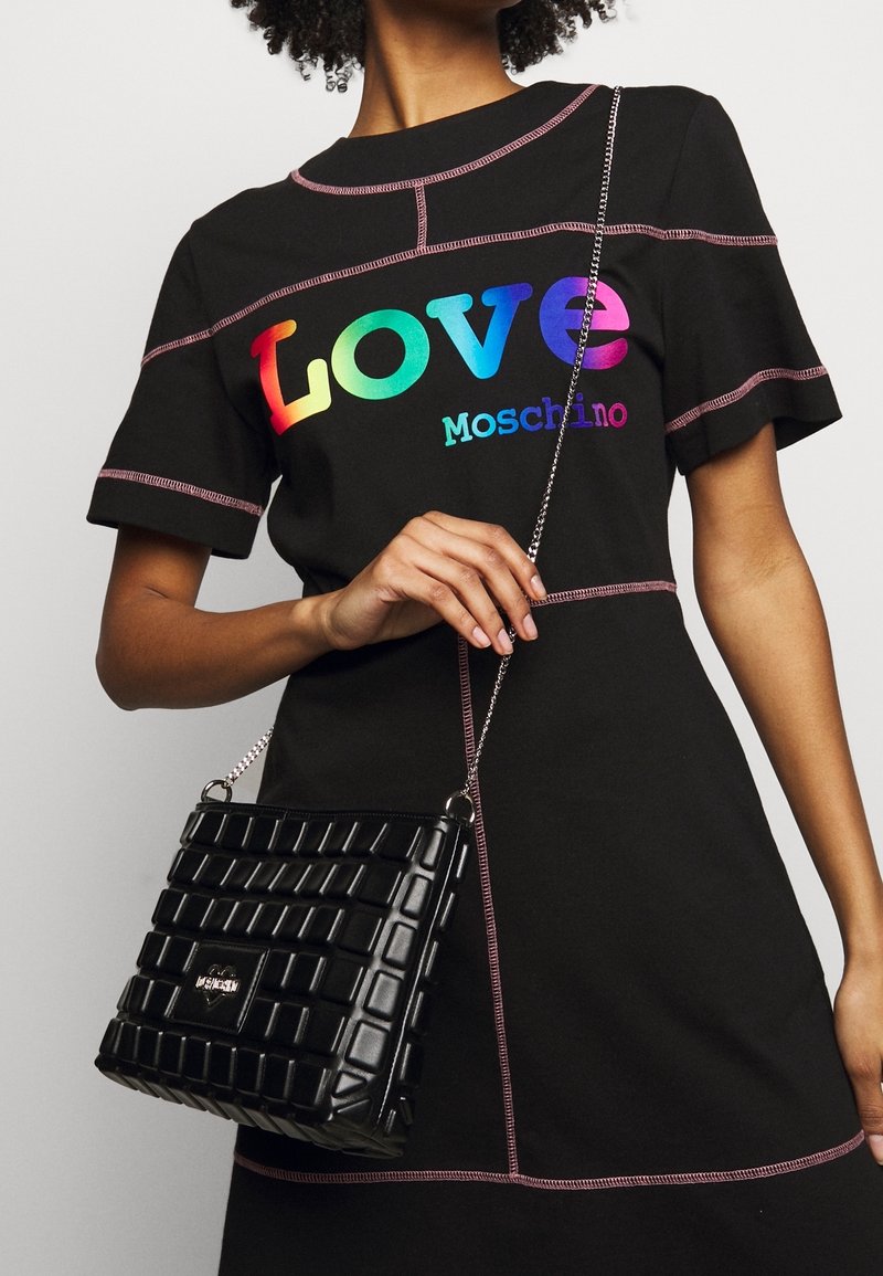 Black short-sleeve dress with pink stitching features a colorful "LOVE Moschino" graphic; paired with a quilted black handbag and chain strap.