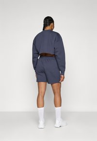 Sweatshirt cropped azul-marinho e calções combinados em um tecido macio e texturizado. Apresenta um cós elástico e um ajuste casual, combinado com meias brancas e sapatilhas.