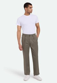 Pantalones de hombre plisados en color verde oliva, fabricados en tejido ligero. Combinados con una camiseta de cuello redondo blanca sin estampados y zapatillas blancas.